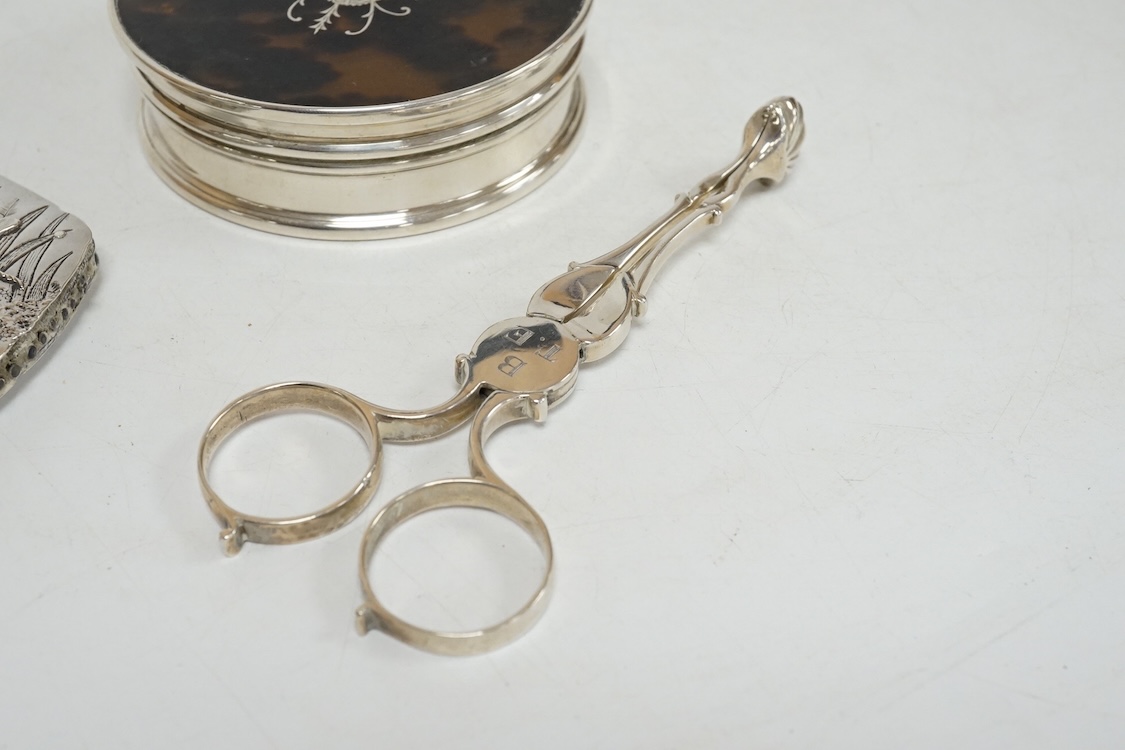 A George V silver and tortoiseshell pique mounted circular trinket box, Collett & Anderson, London, 1922, diameter 77mm, together with a pair of 18th century silver sugar nips and a sterling mounted pin cushion, decorate